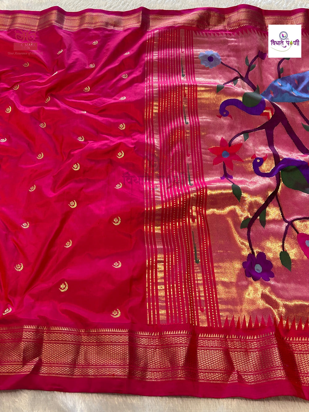 A vibrant magenta pink silk saree with intricate gold zari weaving, featuring a floral and peacock motif on the pallu end.
