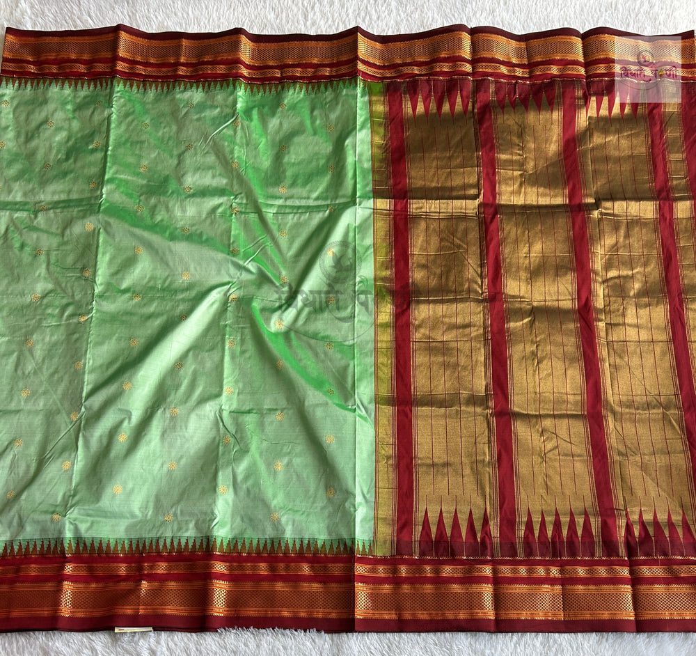 A green silk saree with gold zari motifs and a wide red and gold border, laid flat on a white textured surface.