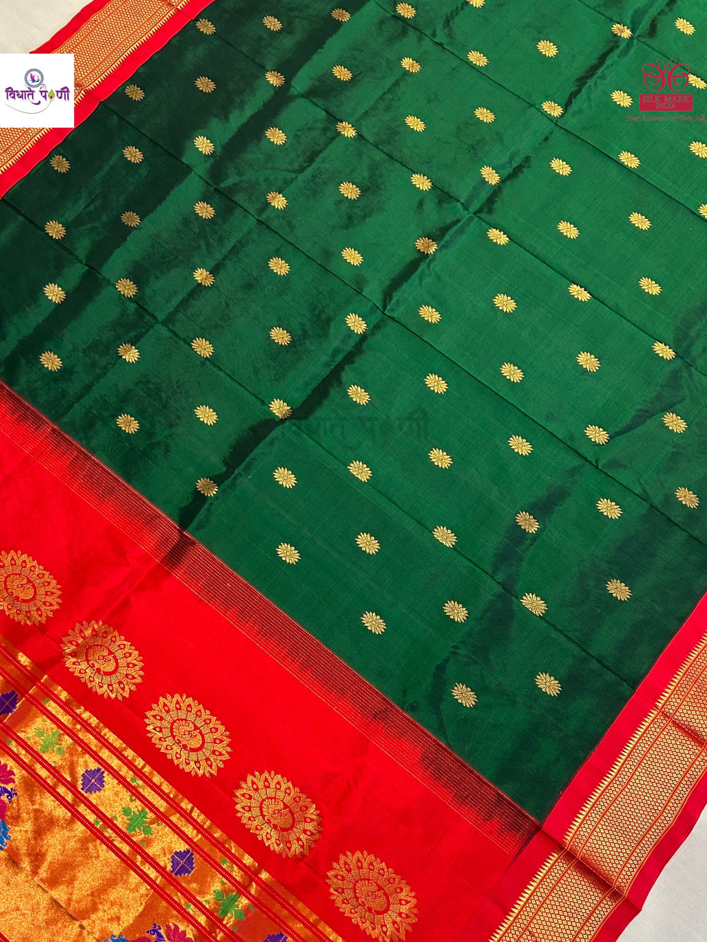 A dark green silk saree with small gold zari motifs and a vibrant red border featuring gold floral patterns and a gold zari pallu.