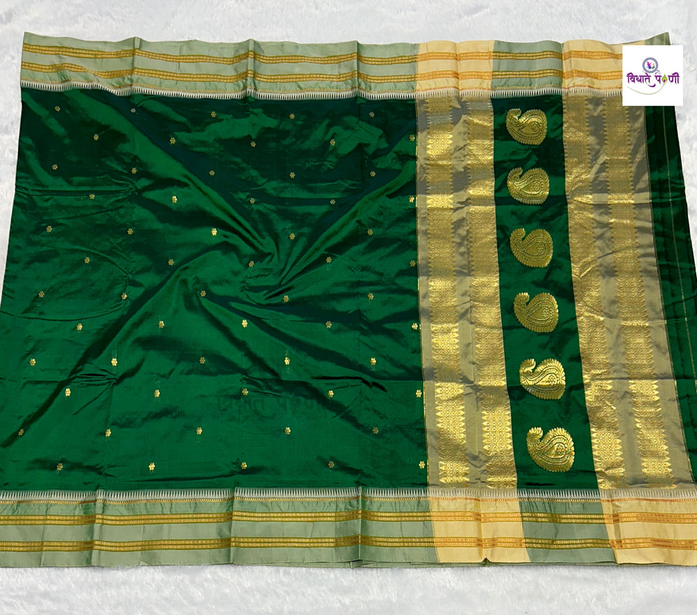 A dark green silk saree with a wide gold and beige zari border, featuring a row of gold paisley motifs and small gold dots on the body, laid flat on a white textured background.