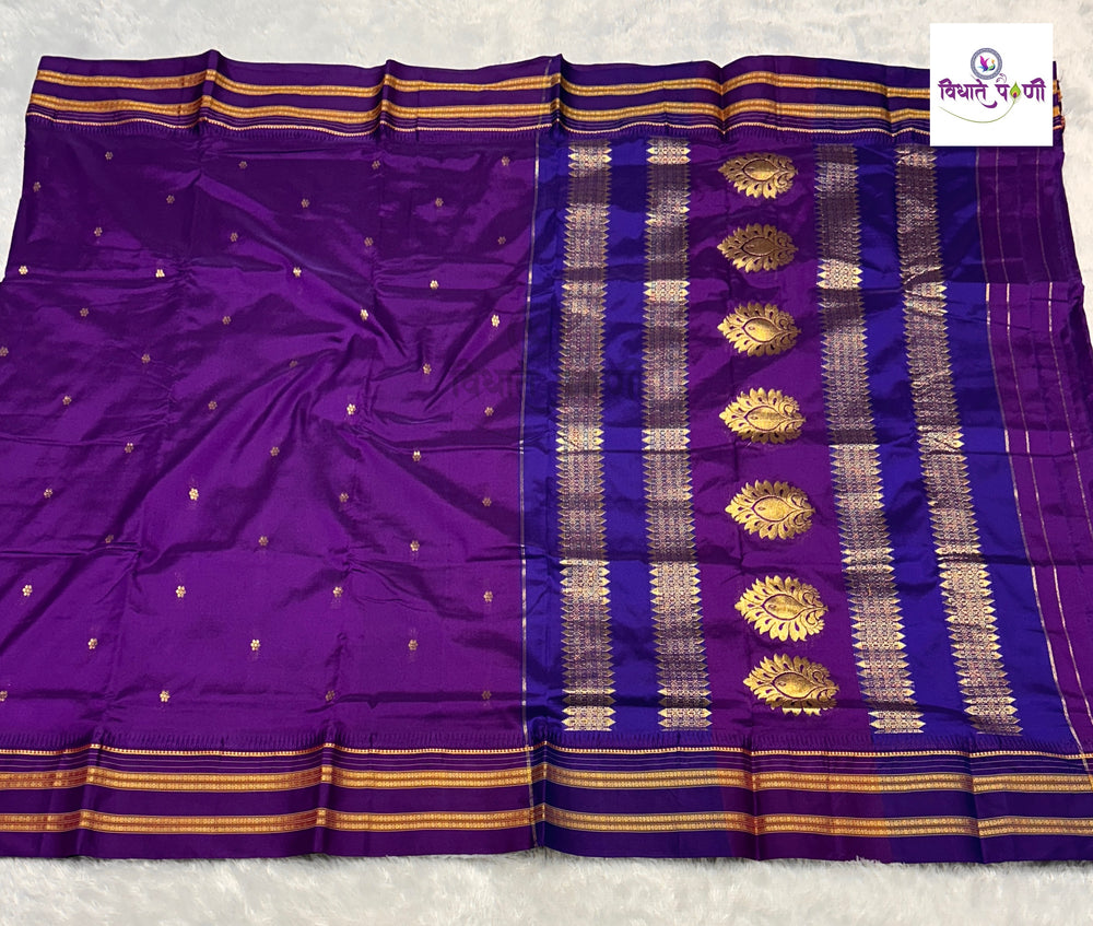 A purple silk saree with gold zari woven borders, gold motifs, and small gold dots, displayed flat on a white textured surface.