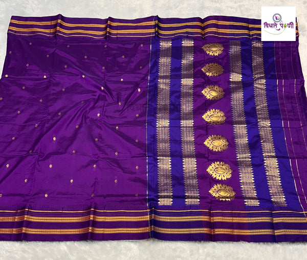 A purple silk saree with gold zari woven borders, gold motifs, and small gold dots, displayed flat on a white textured surface.