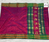 A purple silk saree with a wide green and gold zari border, laid flat on a white textured surface. The border features a vertical row of gold zari paisley motifs and striped borders.