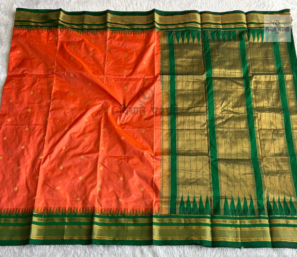 A traditional Indian silk saree laid flat, featuring a vibrant orange body with small gold motifs, a rich green and gold zari border, and a matching green and gold pallu.