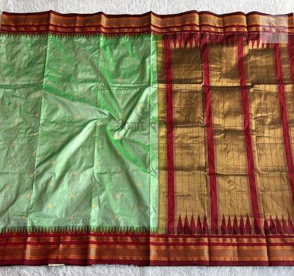 A green silk saree with gold zari motifs and a wide red and gold border, laid flat on a white textured surface.