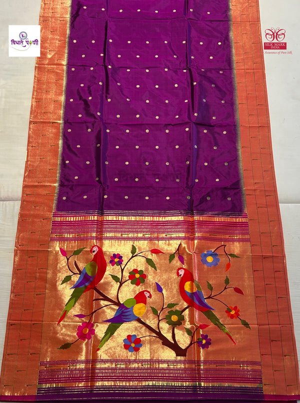 A purple silk saree with a wide orange-gold border, decorated with small gold dots and a colorful embroidered bird and floral motif near the pallu.