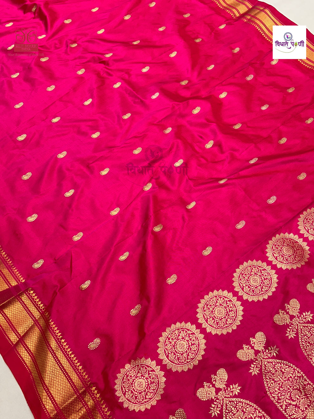 A bright pink silk saree with gold zari woven motifs, featuring a border of large floral and paisley patterns and small scattered motifs across the body.