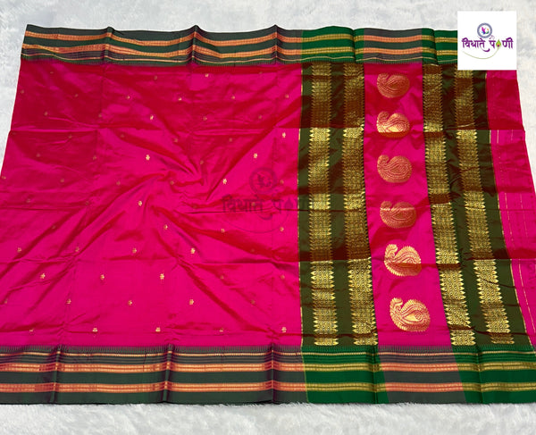 A vibrant pink silk saree with a wide green and gold zari border, laid flat on a white textured surface. The border features metallic gold paisley motifs and striped accents.