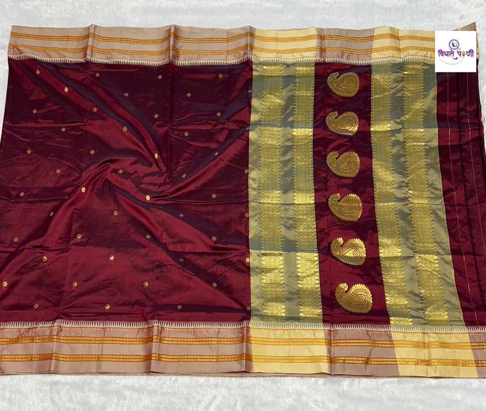 A deep maroon silk saree with gold zari borders, a vertical band of gold paisley motifs, and small gold dots on the body, laid flat on a white textured surface.