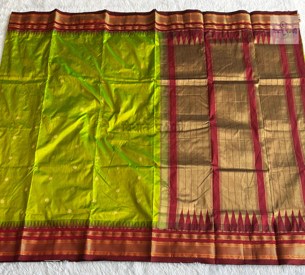 A green and gold silk saree with a red and gold border, laid flat on a white textured background.