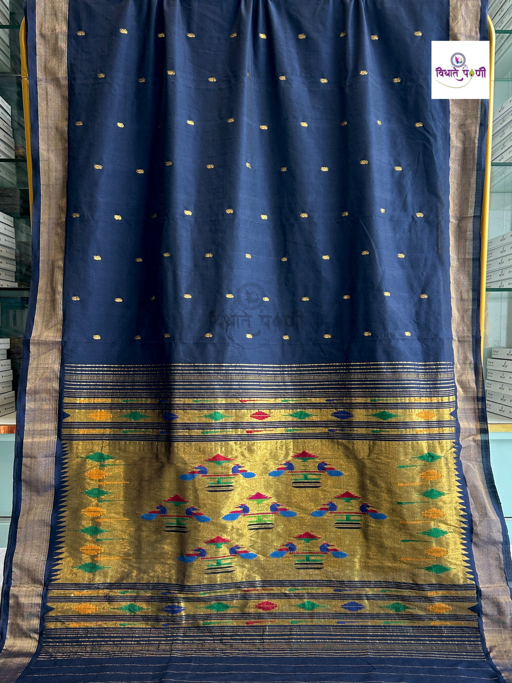 A navy blue silk saree with a wide gold zari border and a highly detailed multicolor ikat pattern in the pallu, displayed against a blurred background.
