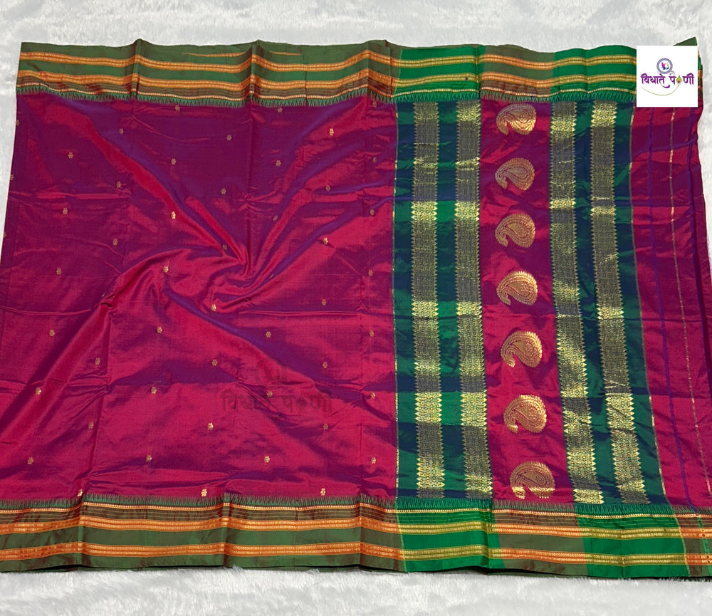 A purple silk saree with a wide green and gold zari border, laid flat on a white textured surface. The border features a vertical row of gold zari paisley motifs and striped borders.