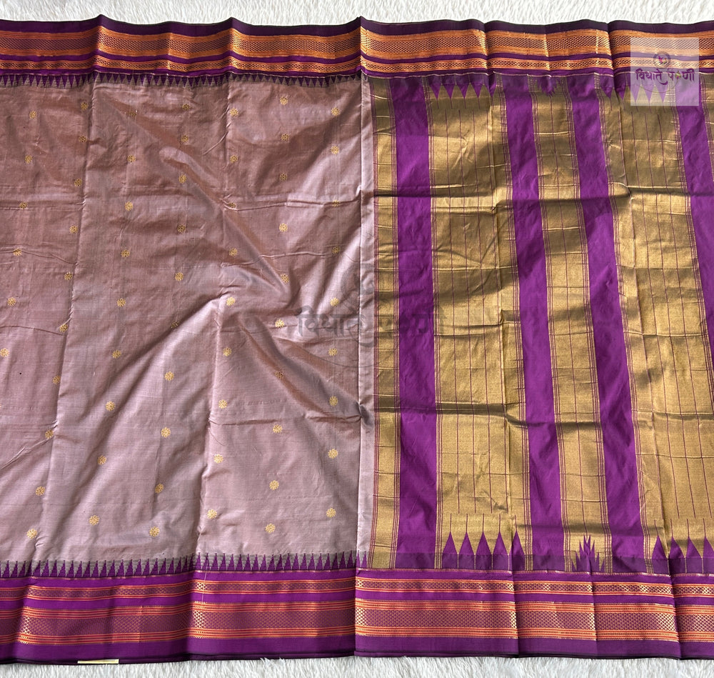 A traditional Indian silk saree laid flat, featuring a dusty mauve body with small gold motifs, a wide purple and gold zari border, and a decorative end pallu.